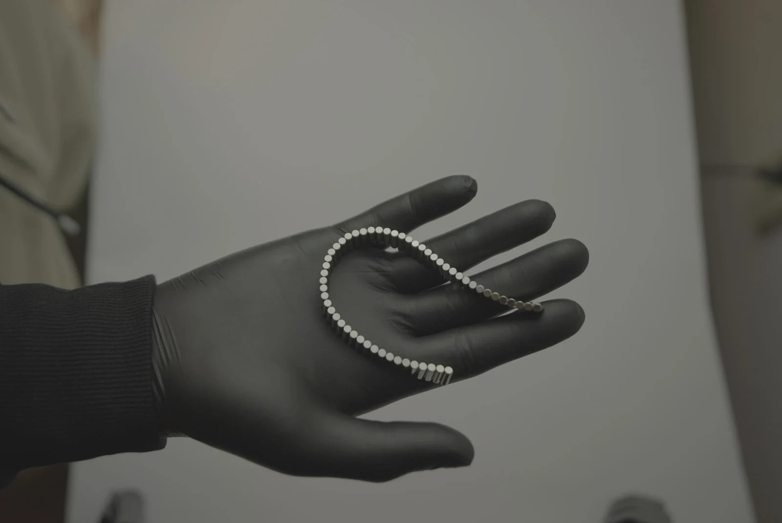 An open silver magnetic bracelet held in a gloved hand